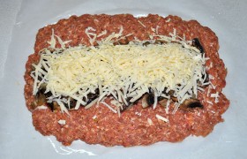 Если фарш у нас домашний – он плотный, поэтому для сочности добавляем немного молока, снова вымешиваем и 20-22 раза  отбиваем . На промазанном маслом пергаменте или фольге разминаем массу прямоугольником 12-15 мм толщины, посередине выкладываем грибы и натираем крупно сыр.