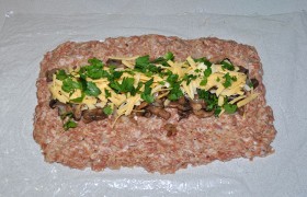 Кладем на стол кусок пленки, смазываем маслом. На нем разминаем фарш в лепешку прямоугольной формы, толщина которой примерно 16-18 мм. Выкладываем грибы и сыр (плавленый или тертый твердый), зелень.