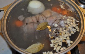 Ставим на огонь большую кастрюлю, в которую легко поместится мясо. Когда закипит, переводим на малый огонь и закрываем крышку. Но перед этим стоит пошевелить кусок, не то кожа может прилипнуть к дну кастрюли. Спустя примерно час добавляем в бульон очищенную луковицу, корень петрушки, чеснок, крупно нарезанную морковь, соль, перец горошком и лавровый лист.