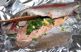 На большой лист фольги, положенный на противень, насыпаем около половины крупно порубленной  петрушки , кладем на нее рыбину. Остальную петрушку и мелко нарезанные 3-4 дольки лимона (с кожей) помещаем в брюшко.