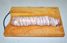 Чуть наискось плотно оборачиваем вырезку ломтиками бекона. Слегка посыпаем перцем.