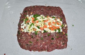 Расстилаем и чуть смачиваем пищевую пленку, разминаем на ней фарш пластом. На середину выкладываем начинку с рубленой зеленью.