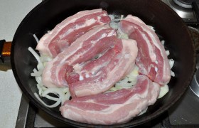 На среднем огне  разогреваем в сковороде масло. Распределяем на дне около половины лука, на него выкладываем ломтики грудинки.